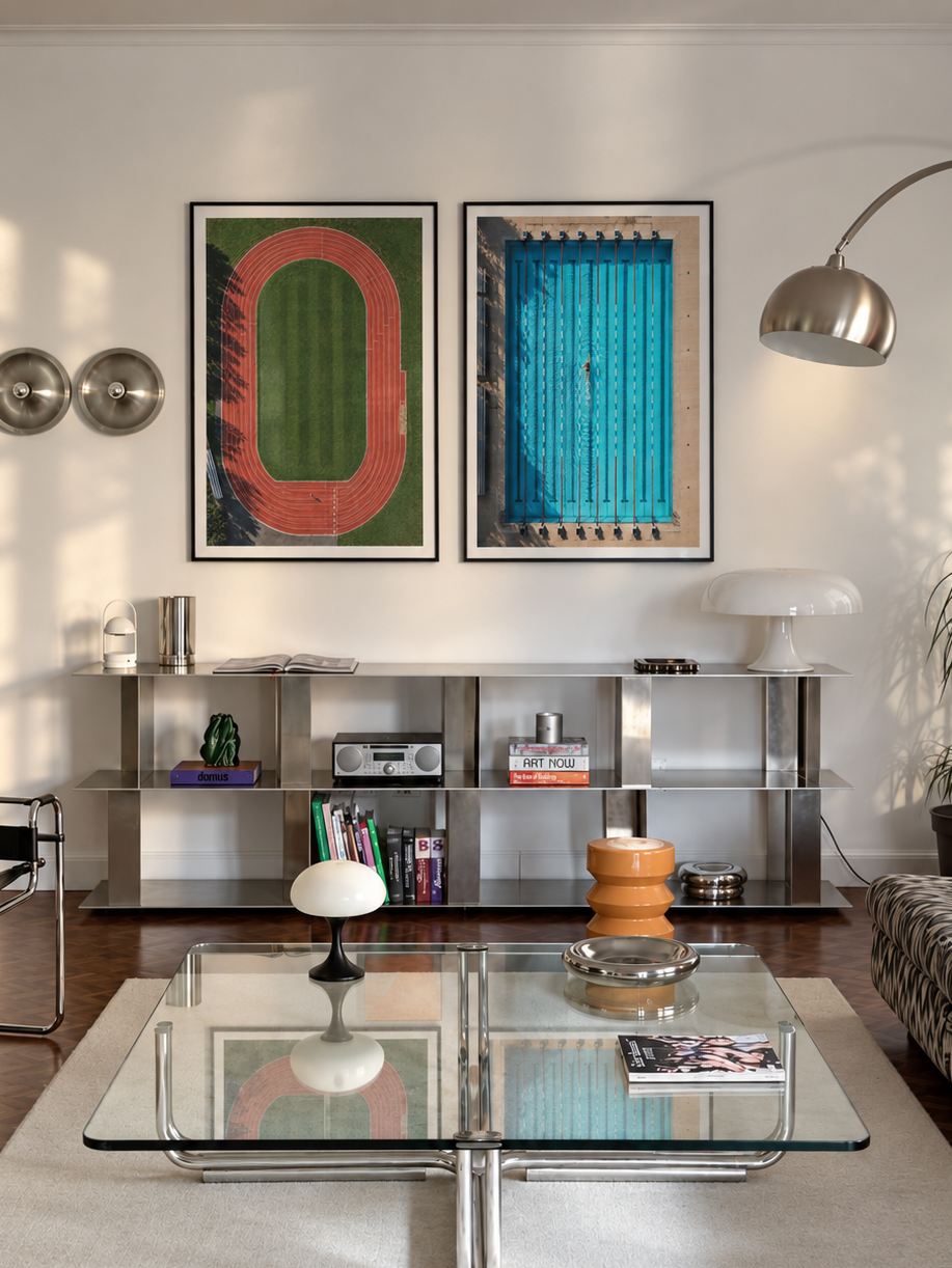 A modern living room featuring two framed abstract art prints hanging on a white wall above a glass coffee table. The prints display a green and red geometric design on the left and a blue vertical striped design on the right.