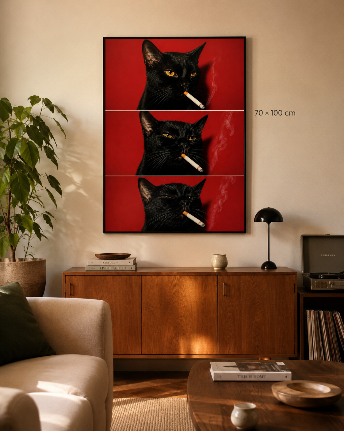 A framed wall art print showing three stacked close-up portraits of a black cat against a vivid red background, each holding a cigarette with visible smoke. The artwork is displayed in a real living room above a wooden cabinet, with a sofa, plant, lamp, and record player visible.